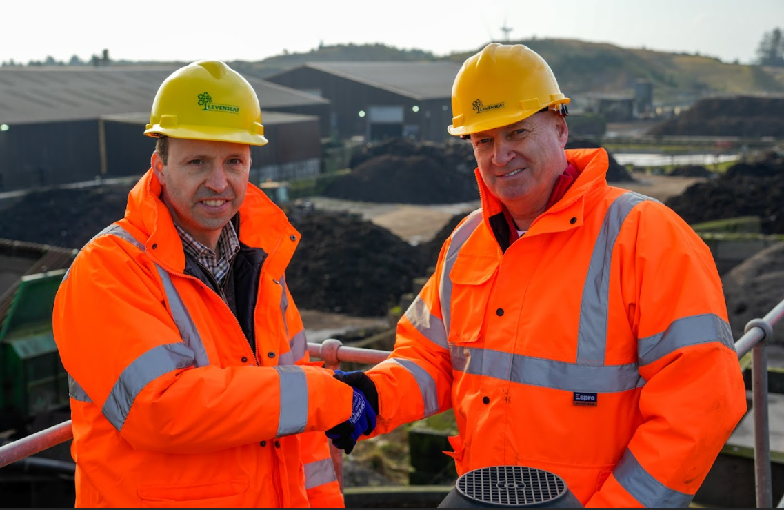 Two White middle-aged men wearing orange high vis clothing shaking hands